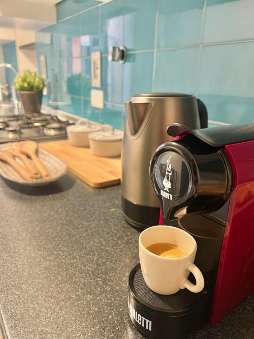 Macchinetta Bialetti che prepara espresso nella cucina di un appartamento bolognese con schienale in vetro turchese