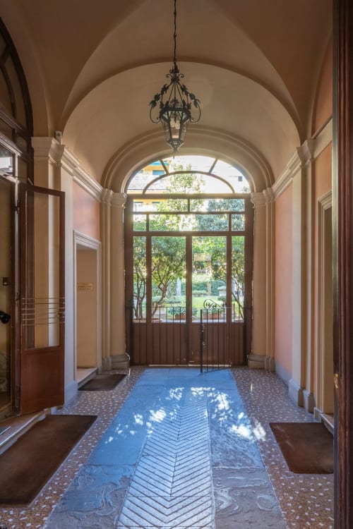 Elegante corridoio con volta a botte, piastrelle a spina di pesce, lampadario ornamentale e vista sul giardino attraverso ampie porte