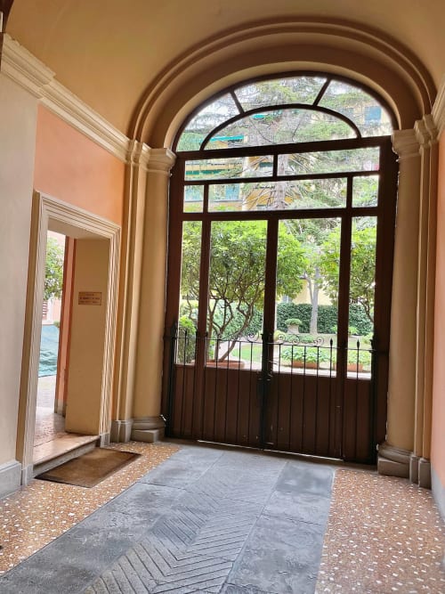 Elegante ingresso ad arco con porte in legno scuro che si aprono su un rigoglioso giardino presso Living Palazzi Storici, appartamento a Bologna