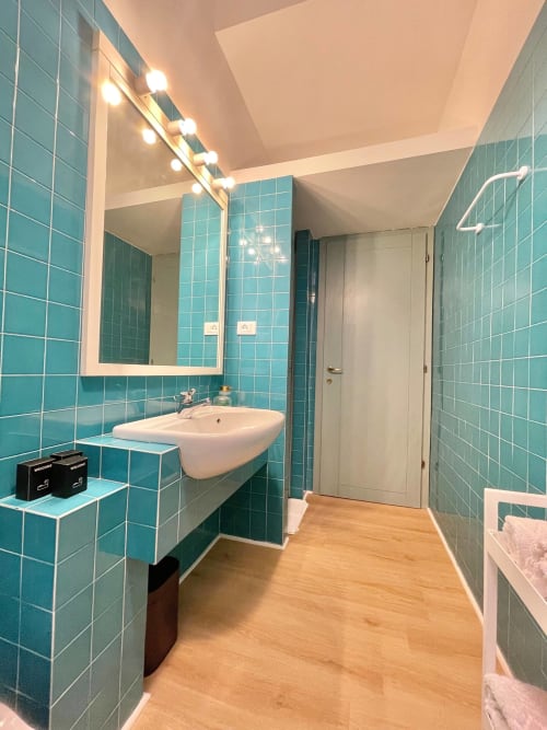 Bagno moderno con piastrelle turchesi, lavabo da appoggio e specchio illuminato nell'appartamento Living Palazzi Storici a Bologna