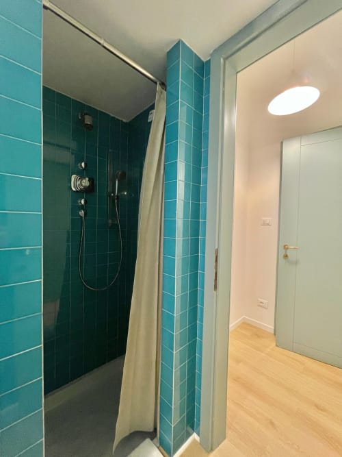 Bagno con doccia in piastrelle turchesi, tenda bianca e pavimento in legno nell'appartamento Living Palazzi Storici, Bologna