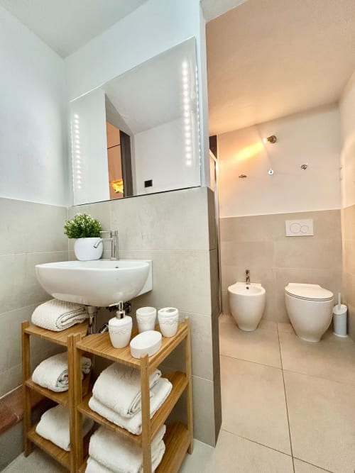 Bagno moderno nell'appartamento Living Palazzi Storici Bologna con specchio illuminato, mensola in legno, bidet, wc e finiture color crema