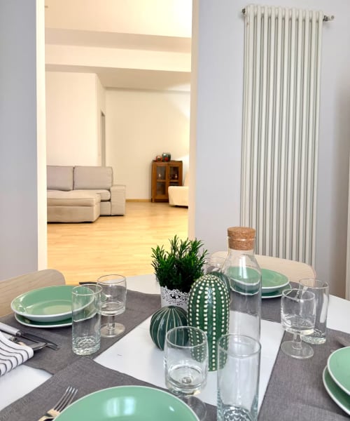 Zona pranzo di Living Palazzi Storici Bologna con sottopiatti verdi, composizione di cactus e vista sul soggiorno