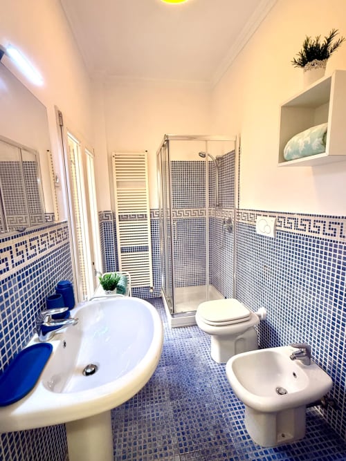 Bagno moderno con piastrelle mosaico blu, sanitari bianchi e doccia in vetro nell'appartamento Santo Stefano, Bologna