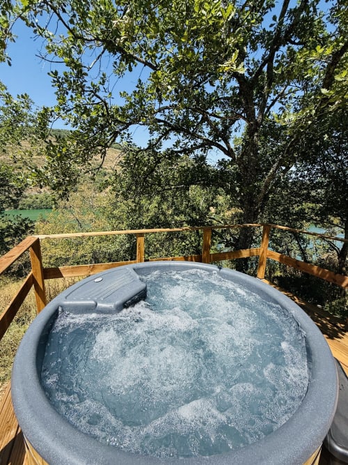 Bain à remous bouillonnant sur une terrasse en bois avec vue sur le lac verdoyant et les arbres de Cabanes et lodges du Belvédère