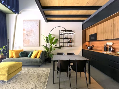 Loft moderno Jenner a Milano con divano giallo, tavolo da pranzo, soffitto in legno, cucina aperta e vista giardino interno.