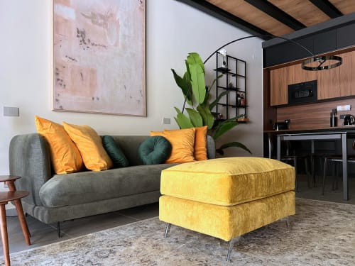 Moderno loft a Milano con divano grigio, pouf giallo, cuscini arancioni e piante verdi