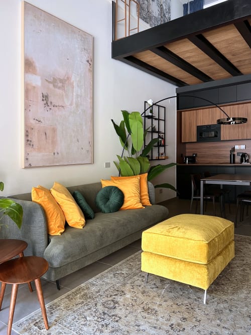Elegante soggiorno in stile loft a Milano con divano grigio, pouf giallo, cuscini arancioni e arte murale astratta