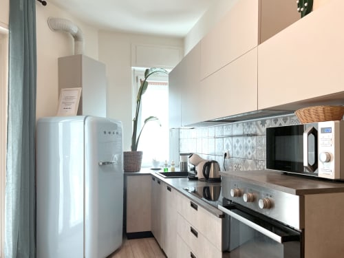 Cucina moderna nell'appartamento Nestco Milano con frigorifero SMEG bianco, fornello, microonde e rivestimento decorativo
