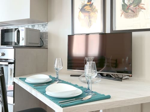 Zona cucina-sala da pranzo moderna nell'appartamento Nestco Milano con tavola apparecchiata, bicchieri di vino e TV a schermo piatto sopra il bancone