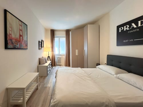 Camera da letto luminosa a Milano con letto matrimoniale, testata scura, arredi beige, accesso al balcone e comfort moderni