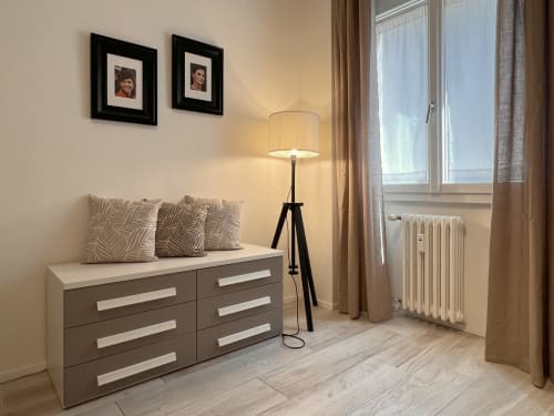 Appartamento Nestco Milano The Quiet Bausan: camera da letto moderna con comò, cuscini decorativi, lampada da terra, ritratti incorniciati e