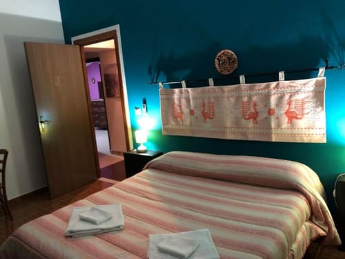 Ampia camera matrimoniale al B&B Daddanca di Ales con biancheria a righe, pareti turchesi e vista sulla corte interna