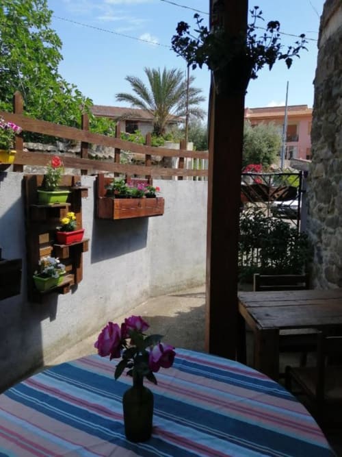 Soleggiata corte del B&B Daddanca ad Ales con rose viola, fioriere in legno e architettura mediterranea tradizionale
