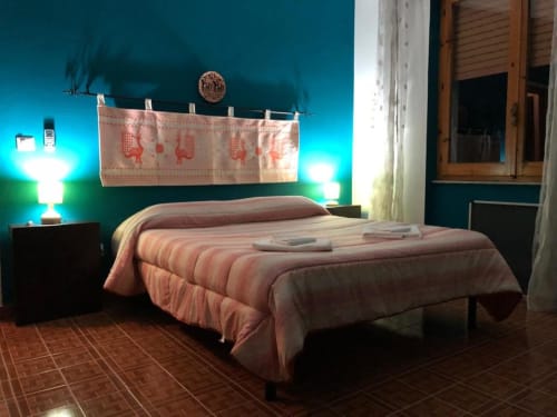 Camera da letto al B&B Daddanca di Ales con pareti turchesi, biancheria rosa, lampada decorativa e porta rustica in legno