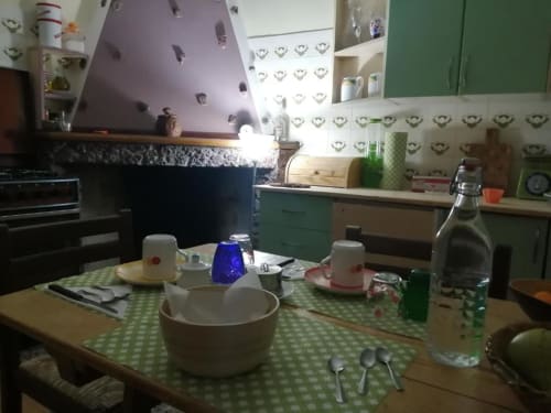 Area cucina del B&B Daddanca ad Ales con tavolo da pranzo, elettrodomestici e arredamento a quadri verdi nella stanza della corte interna.