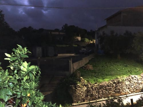 Cortile interno al tramonto, B&B Daddanca ad Ales con edifici illuminati, muri in pietra e lussureggiante vegetazione