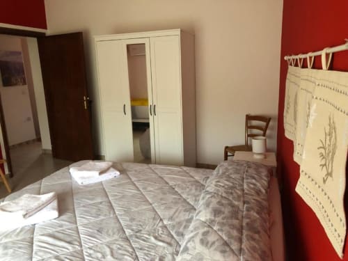 Ampia camera matrimoniale a B&B Daddanca ad Ales con letto, guardaroba bianco e parete accent rossa
