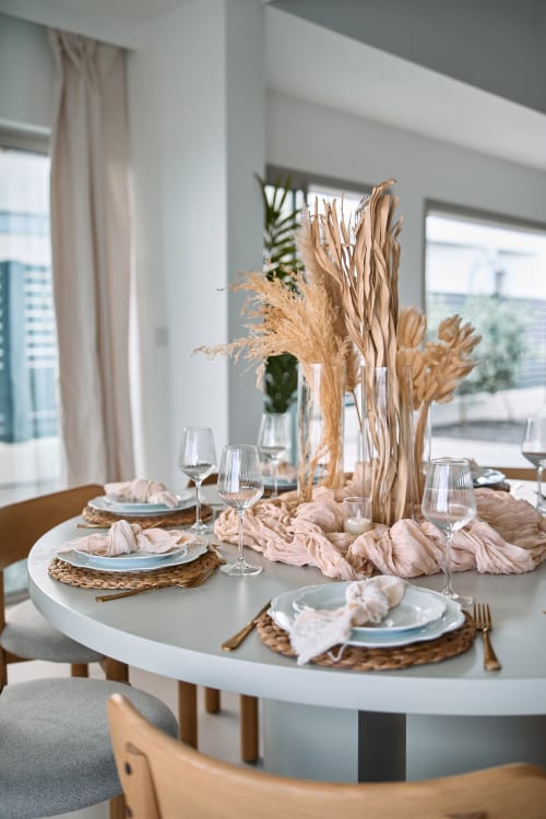 Table de salle à manger ronde élégante à l'hôtel Maly Blue Location avec centre de table en pampas séchées, couverts et vue océan au