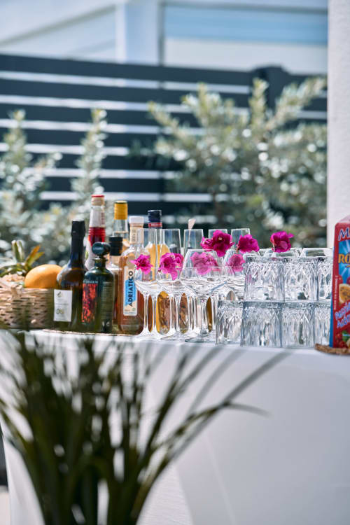 Bar extérieur à l'hôtel Maly Blue Location au Moule avec verres à vin, bouteilles, fleurs roses et plantes tropicales