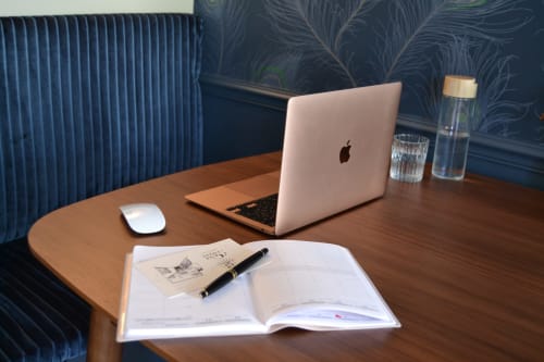 Espace de travail moderne à L'ODE A PIERRE B&B à Dax avec bureau en bois, MacBook, carnet et verres d'eau