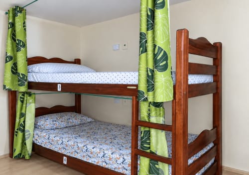 Dormitório compartilhado com beliches de madeira e cortinas verdes no Hostel New Ipanema, Rio de Janeiro