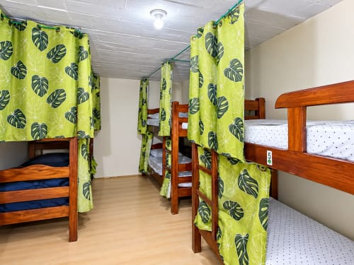 Quarto compartilhado do Hostel New Ipanema com beliches de madeira, cortinas verde-lima estampadas de folhas e banheiro compartilhado no Rio de Janeiro