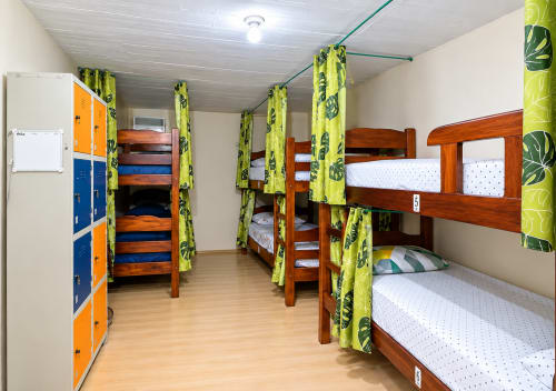 Mixed dormitory room at Hostel New Ipanema in Rio de Janeiro with wooden bunk beds, lime green curtains, and lockers