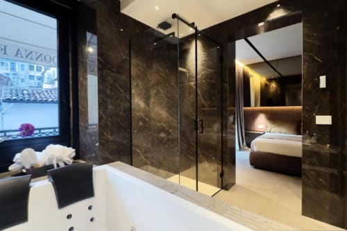 Lussuoso bagno a Donna Filomena con pareti in marmo, box doccia in vetro, vasca idromassaggio e vista sulla città in hotel italiano