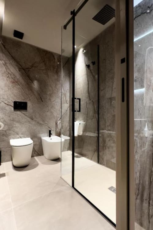 Bagno moderno nelle Luxury Suites Donna Filomena con pareti in marmo grigio, WC e bidet bianchi, doccia walk-in con dettagli neri