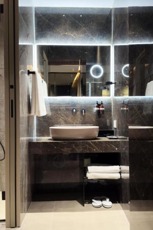 Bagno di lusso moderno a Donna Filomena con pareti in marmo scuro, specchio retroilluminato a LED, lavabo bianco e servizi in stile italiano