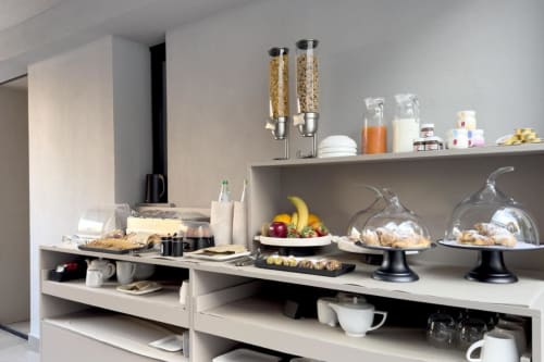 Moderna sala colazioni presso Donna Filomena Luxury Suites con cereali, pasticcini, frutta fresca e bevande su sfondo bianco