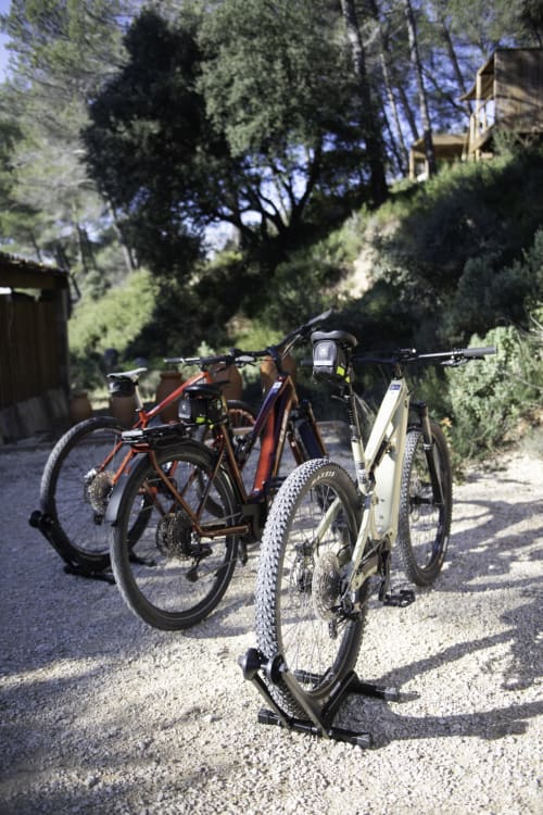 Trois vélos garés sur un chemin de gravier au Chant des pins Lodges & Spas à Saint-Marc-Jaumegarde, avec une colline boisée en arrière-plan