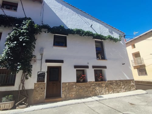 Exterior del apartamento rural Casa El Abuelo en Bronchales: muros blancos, hiedra, base de piedra y puerta de madera