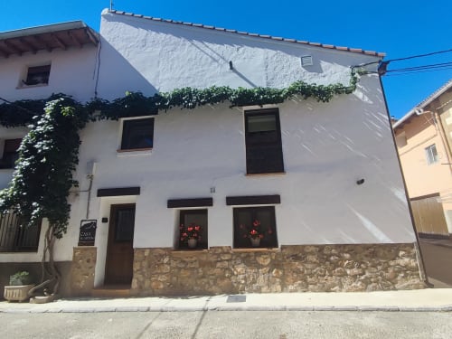 Casa rural El abuelo y Lahuerta en Bronchales - casita de piedra blanca con puertas y ventanas oscuras, fachada cubierta de hiedra, clara