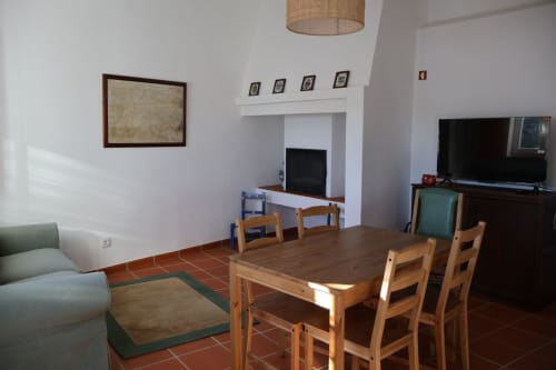 Spacious living area at Herdade Do Vidigal with wooden dining table, fireplace, TV, and green sofa in Montemor-o-Novo