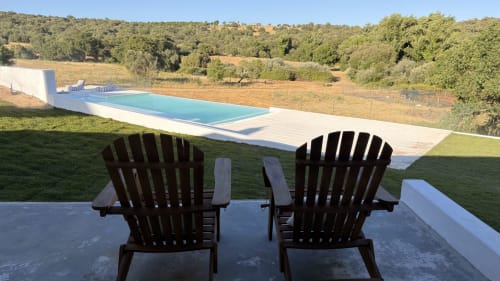 Two black Adirondack chairs overlook a turquoise pool and countryside at Herdade Do Vidigal in Montemor-o-Novo, Portugal