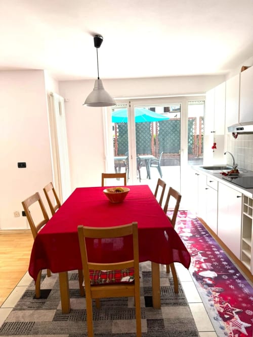 Zona cucina-pranzo moderna della casa Debby Siusi con tovaglia rossa, sedie in legno e vista terrazza sui monti Siusi