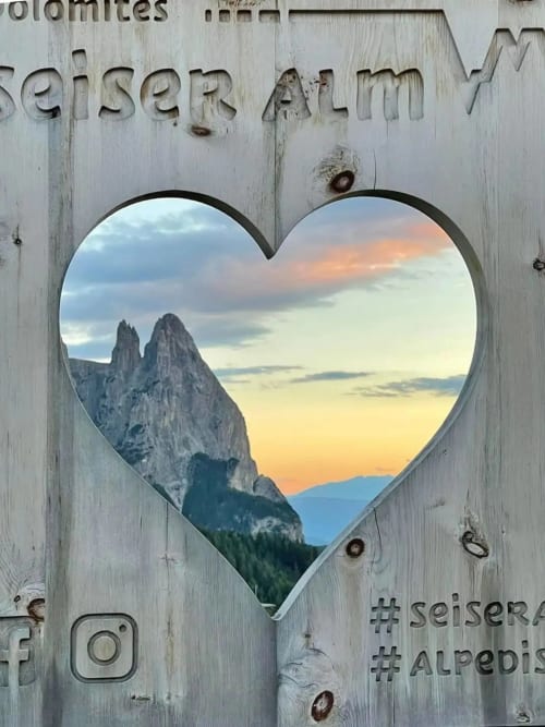 Finestra a forma di cuore che incornicia i picchi delle Dolomiti al tramonto, Alpi di Siusi, casa Debby Siusi