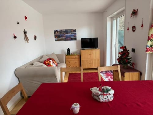 Accogliente salotto della casa Debby Siusi a Siusi con tavolo rosso, mobili in legno, TV e decorazioni natalizie
