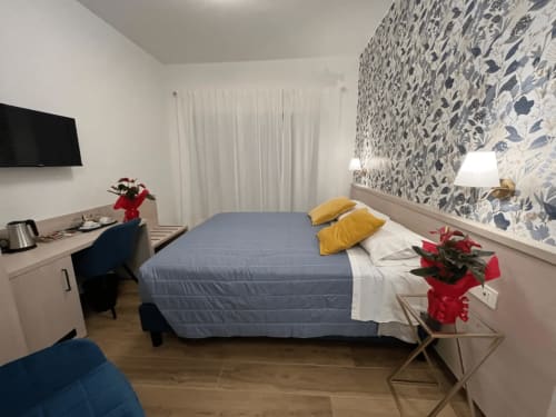 Camera moderna presso Maritza Guest House Roma con letto blu, cuscini gialli, carta da parati floreale e scrivania di lavoro