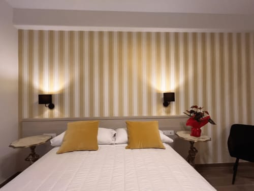 Camera da letto della Maritza Guest House a Roma con carta da parati rigata, letto matrimoniale, cuscini gialli e applique moderne