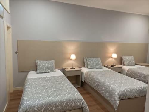 Quarto triplo da Hospedaria Londres Porto com três camas, cabeceira bege, roupa de cama estampada, mesas-de-cabeceira com luminárias e acabamento em madeira
