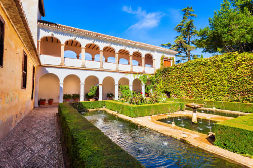 Riad Casa Angelo courtyard in Marrakech with arched columns, water channels, manicured hedges, and clear blue sky
