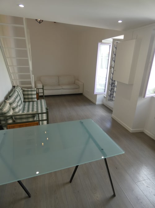 Espace de vie moderne à la résidence Sci Ludji Nanterre avec table en verre, canapé crème, chaises rayées et étagères mezzanine