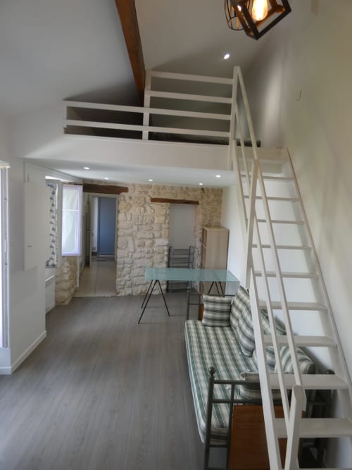 Appartement Sci Ludji avec mezzanine à Nanterre : escalier blanc, table à manger en verre et mur en pierre