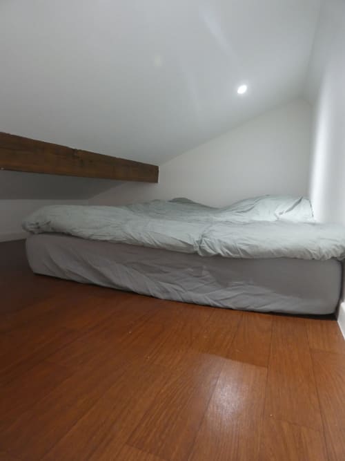 Chambre cosy avec literie blanche sur lit bas, tête de lit en bois, spots encastrés, parquet. Appartement Sci Ludji