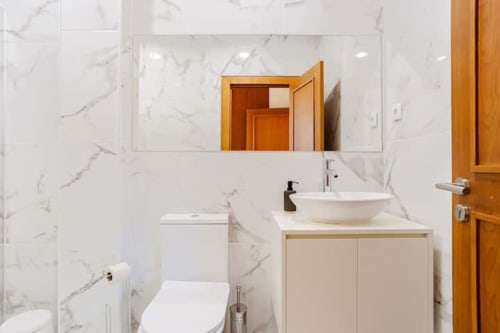 Modern bathroom with white marble tiles, vessel sink, and wooden vanity in Casa dos Vasconcelos cottage, Chaves Portugal