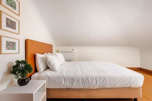 Bright bedroom at Casa dos Vasconcelos cottage in Chaves with orange headboard, white bedding, and framed botanical prints