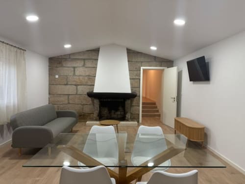 Modern living room at Casa dos Vasconcelos cottage in Chaves with fireplace, glass dining table, gray sofa, and TV